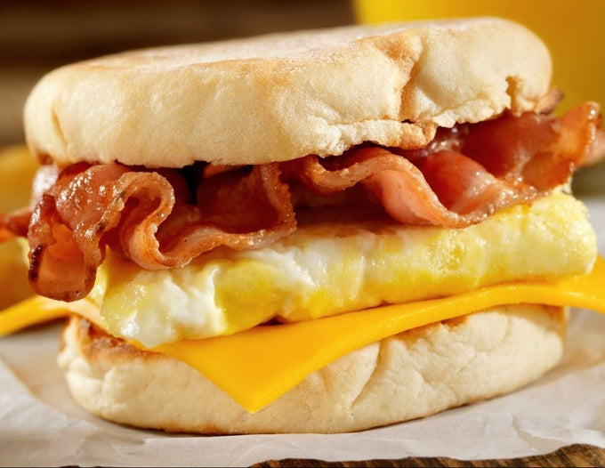 Promotional flyer for a free brekkie with RLA, featuring a close-up photo of a breakfast sandwich with bacon, egg, and cheese, alongside a glass of orange juice and text details for the WDT Trade Centre.